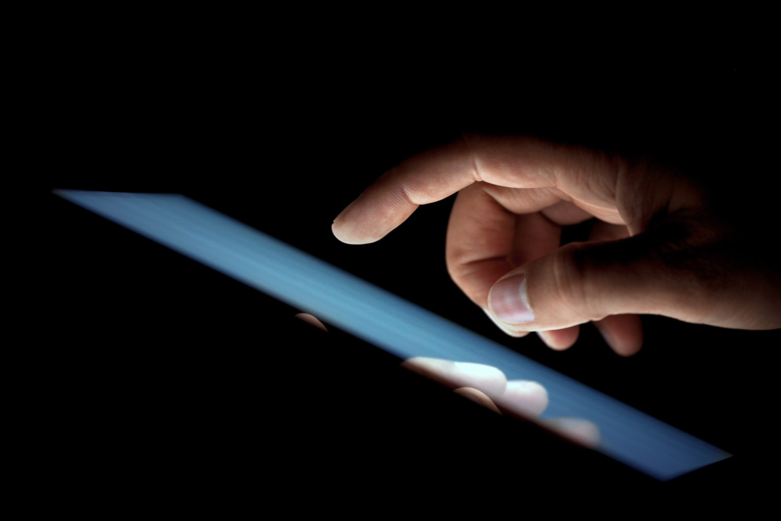 A hand approaches a lit device in a dark room