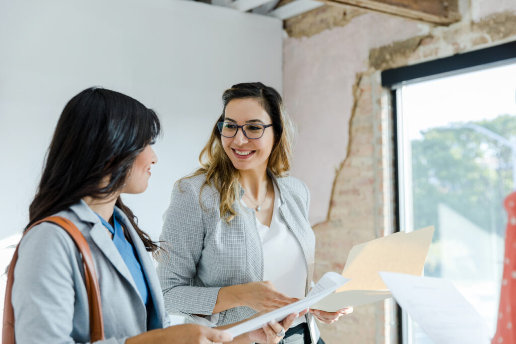 The young adult businesswoman smiles at the real estate broker as they review the paperwork together.