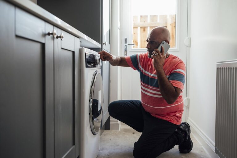 tenant looking at dishwasher that needs repair while on the phone with his landlord
