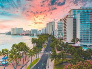 A breathtaking aerial view of Waikiki Beach at sunset with highrise buildings and palm trees lining the shoreline.