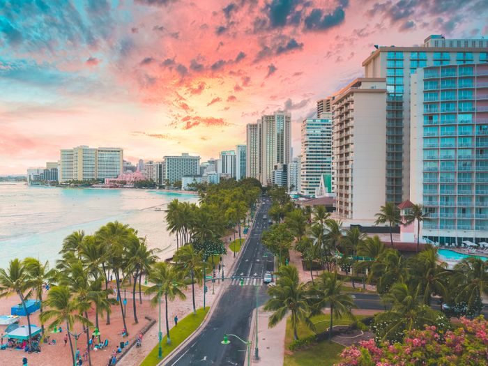 A breathtaking aerial view of Waikiki Beach at sunset with highrise buildings and palm trees lining the shoreline.